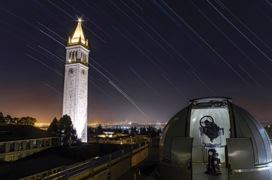 Star trails on pictured behind a telescope and Campanile at UC Berkeley