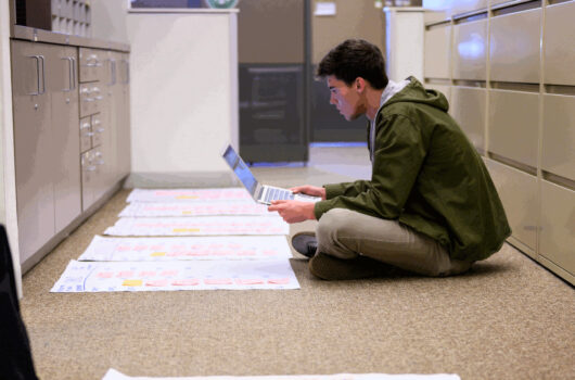 Student researcher with laptop surrounded by posters